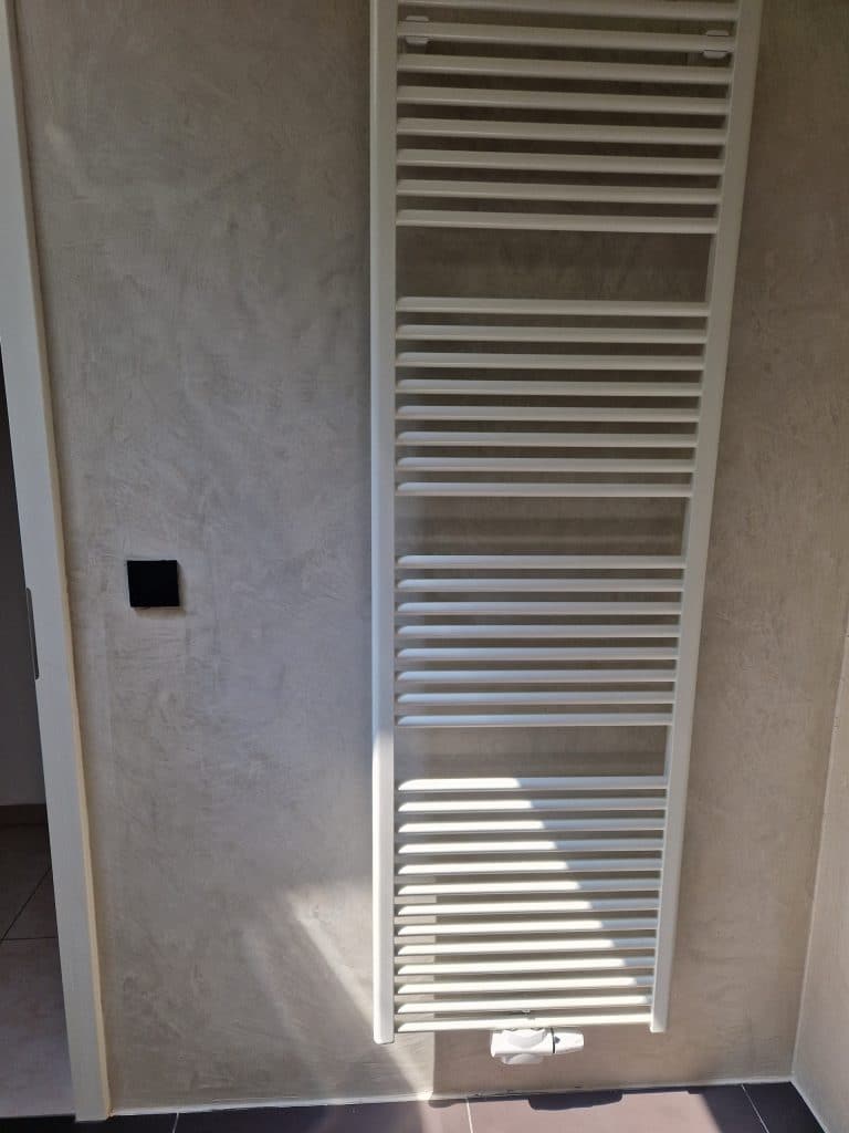 Mur en Mortex gris clair avec sèche-serviettes blanc dans une salle de bain, réalisation Sol Color