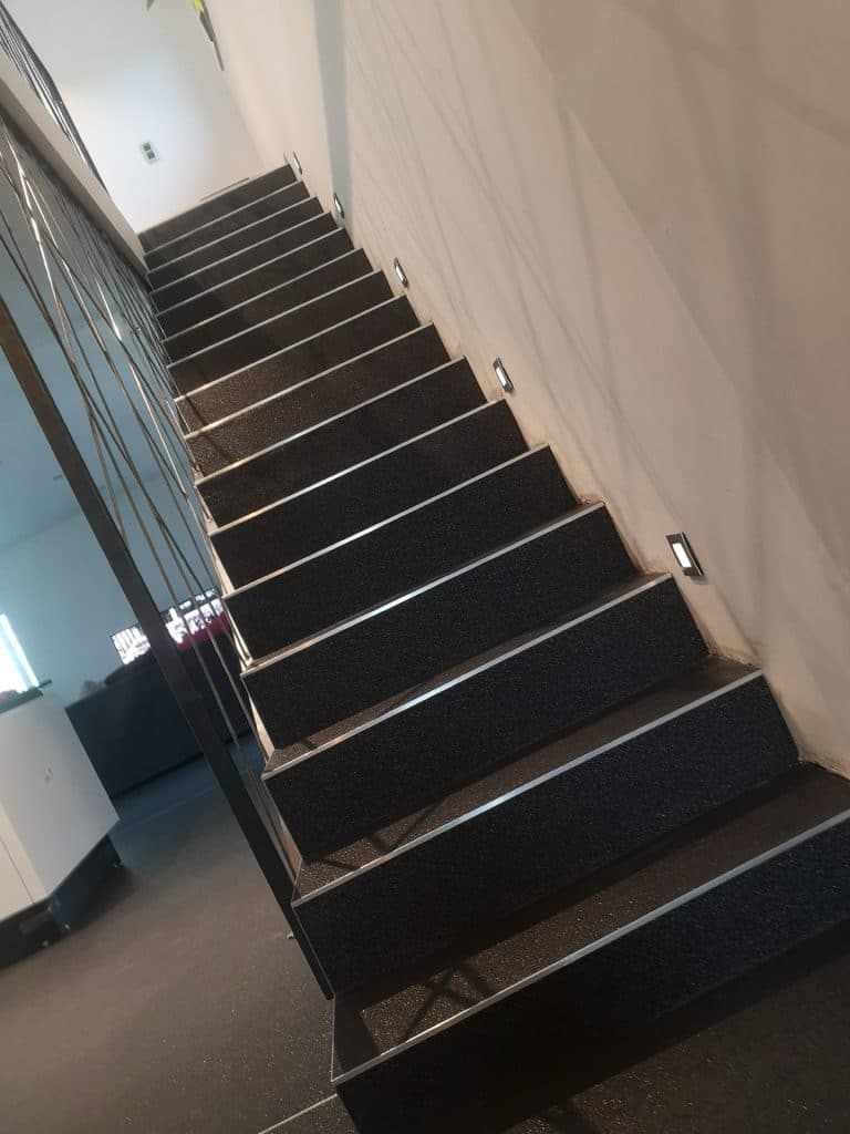 Escalier intérieur habillé de tapis de pierres anthracite avec nez de marche inox et éclairage mural, Sol Color